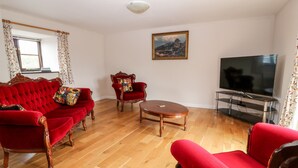 Een woonkamer met een rode bank, een bijpassende fauteuil, een houten salontafel en een televisie op een meubel.
