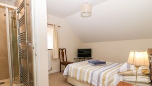 Een slaapkamer met een bed, televisie, lamp en een douchehoek.