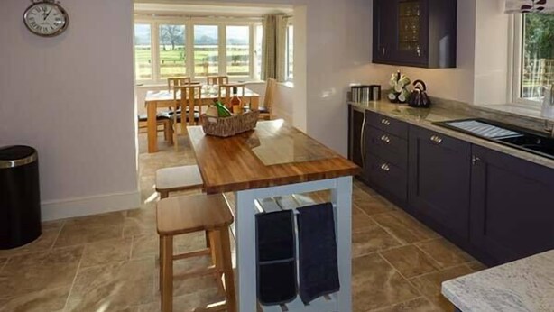 A kitchen with dark cabinets, a wooden island, and a clock on the wall. - Rose Cottage (Hereford)