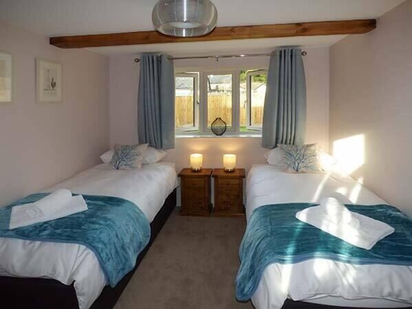A bedroom with two beds, a wooden ceiling beam, a window with curtains, and bedside lamps.