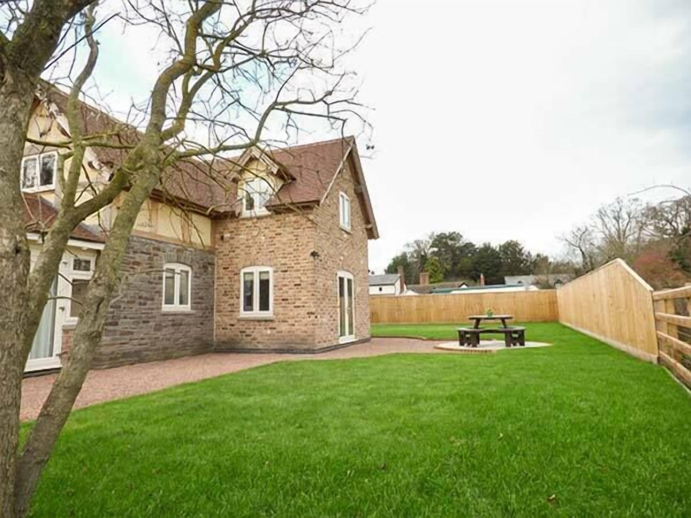 A stone house with a grassy backyard, a wooden fence, and a picnic table.