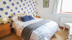A bedroom with a bed, a nightstand, a dresser, a window with curtains, and a framed picture on the wall. - Woodlands (Skipton)