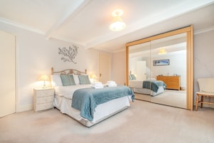 Un dormitorio con cama, mesitas de noche, cómoda, espejo y una silla.
