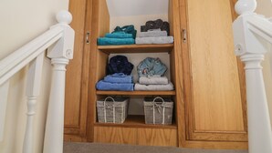 Une armoire en bois dotée de plusieurs étagères, chacune contenant des serviettes pliées et un panier.
