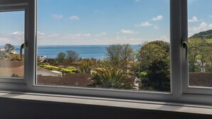 A view through a window with a clear sky, a distant body of water, and a residential area with houses and greenery. - Treverrion (St Austell)