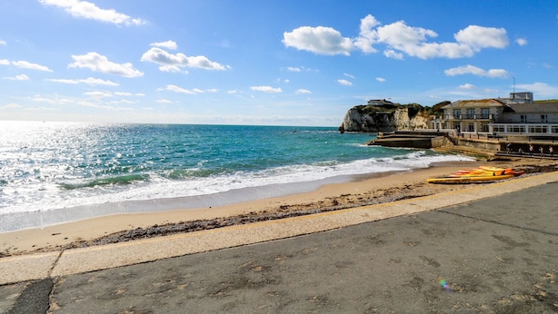 A coastal scene with a clear sky, a sandy beach, and a rocky cliff with a building on top. - Fieldside (Totland Bay)