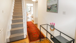 A staircase leading to a room with a red patterned carpet, a glass table with flowers, and a painting of a harbor scene. - Fieldside (Totland Bay)