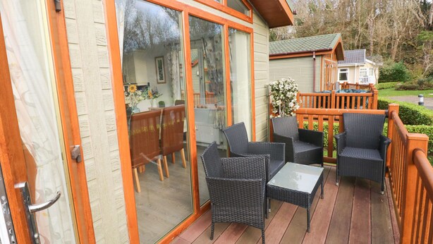 Een terras met rieten meubilair en een glazen deur die leidt naar een binnenruimte met een eettafel en stoelen.