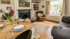 A cozy living room with a fireplace, a dining table set for two, and a comfortable sofa. - Rose Cottage (Bakewell)