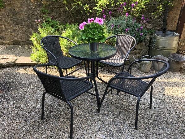 A round table with four black wicker chairs, surrounded by gravel. - Rose Cottage (Bakewell)
