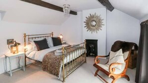 A bedroom with a bed, bedside table, chair, and a fireplace. - Rose Cottage (Bakewell)