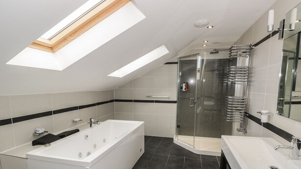 A modern bathroom with a large bathtub, a glass-enclosed shower, and a vanity with a mirror. - Hillside Farm (Kirkby Stephen)