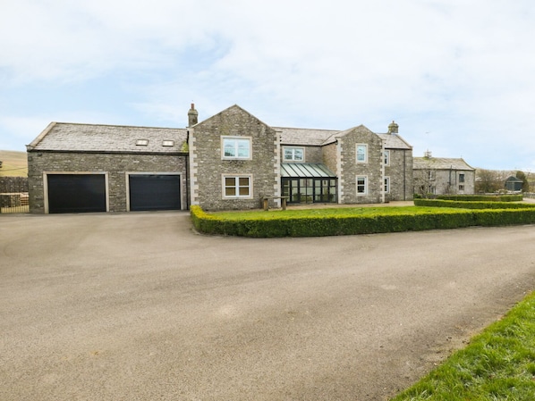A large stone building with multiple garage doors, a conservatory, and a well-maintained lawn.
