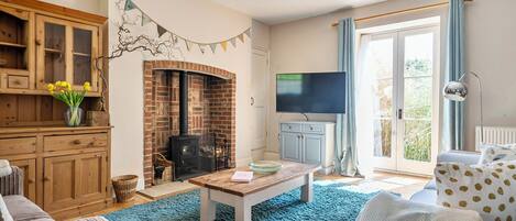 A living room with a brick fireplace, a television, and a large window with curtains.