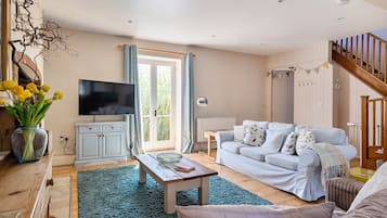 Ein Wohnzimmer mit Fernseher, Sofa, Couchtisch und einer Treppe.
