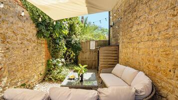 A cozy outdoor seating area with wicker furniture and a glass table, surrounded by stone walls and greenery.