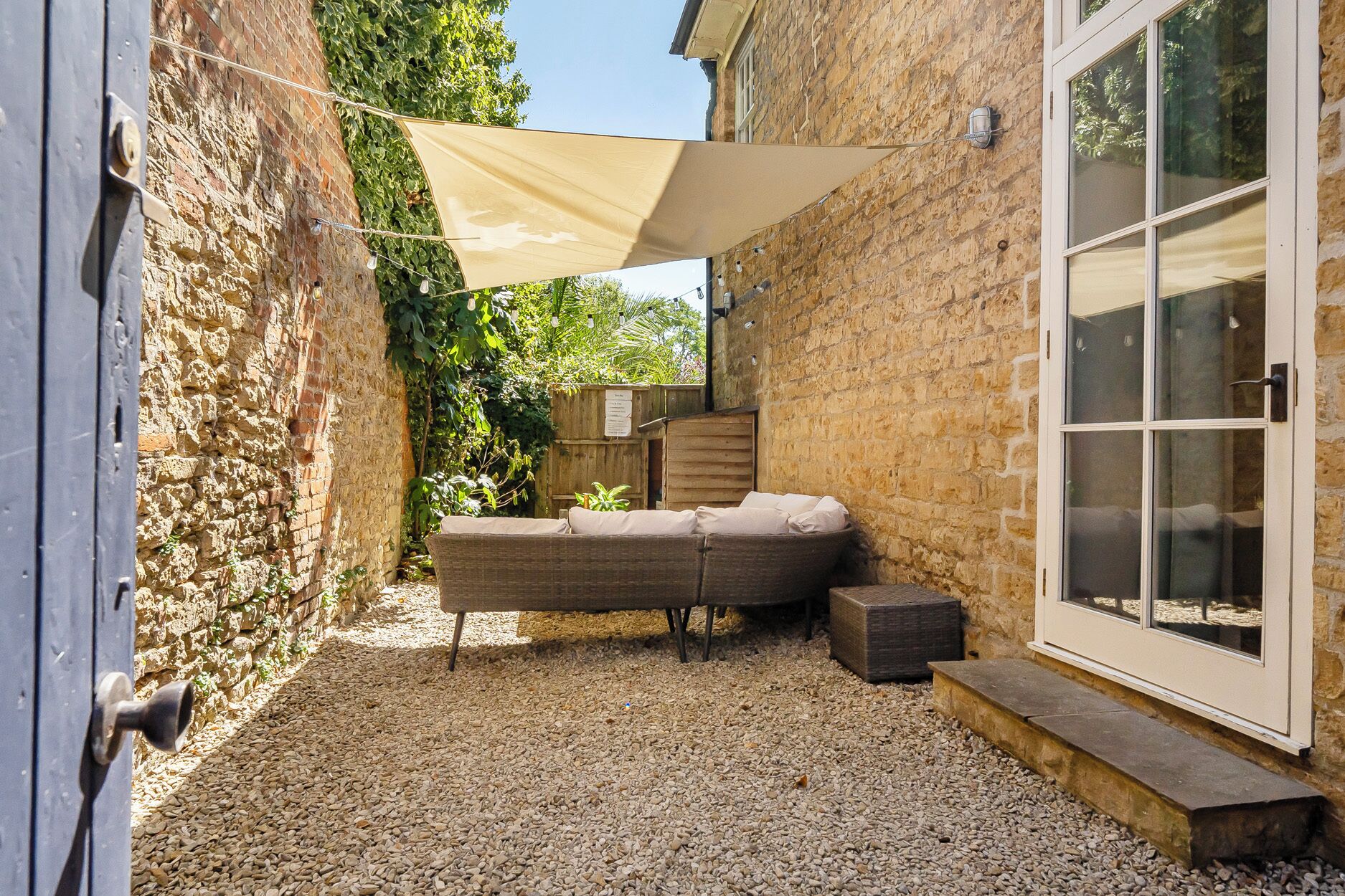 Un patio con un sofá de mimbre, una vela de sombreo color beige y piso de grava.