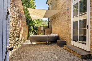 Un espace patio aménagé avec un canapé en osier, une voile d’ombrage de couleur beige et un sol en gravier.