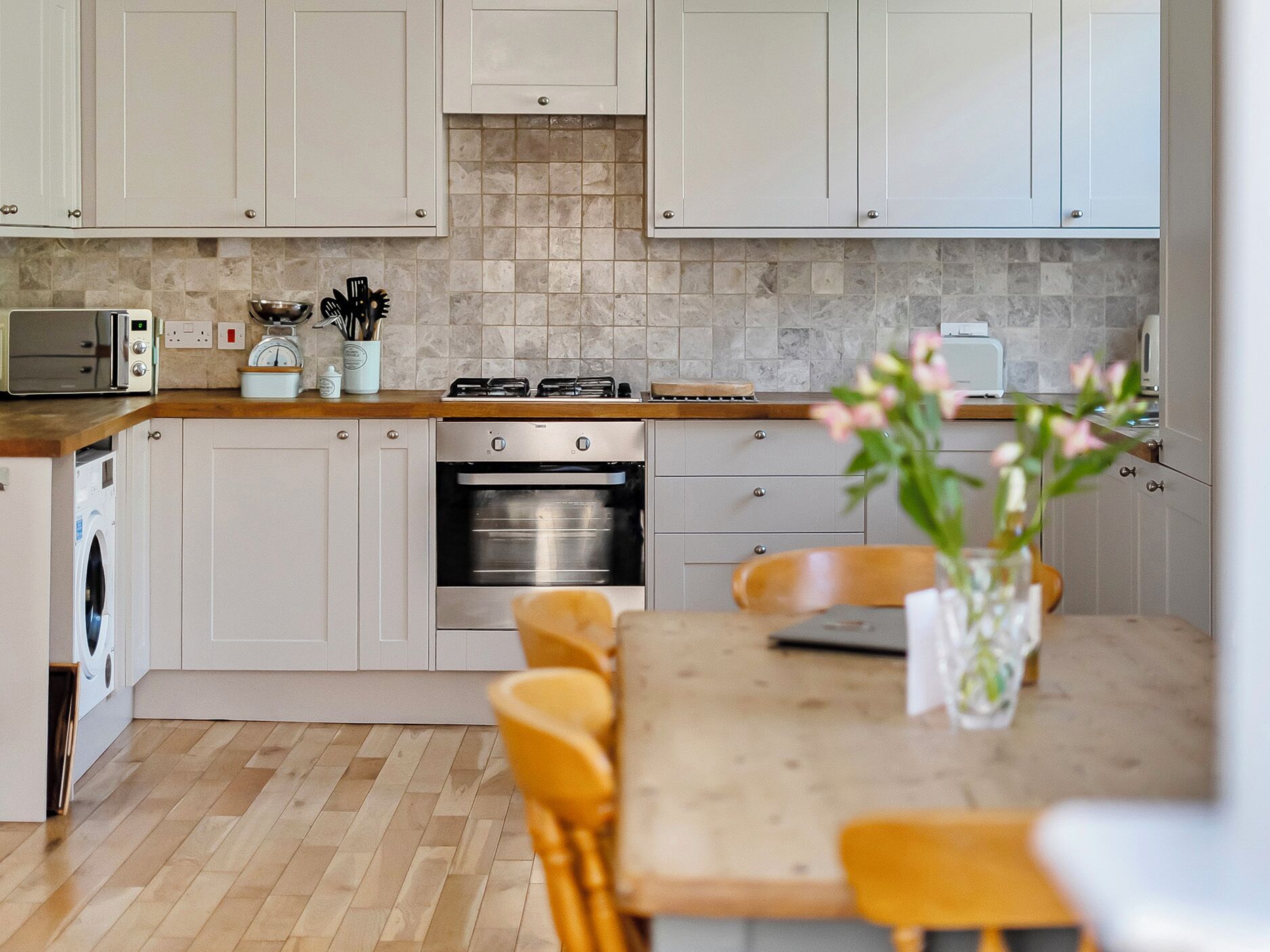 Een moderne keuken met witte kastjes, een houten aanrechtblad, een ingebouwde oven en een eethoek met een tafel en stoelen.