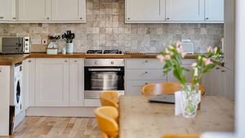 Een moderne keuken met witte kastjes, een houten aanrechtblad, een ingebouwde oven en een eethoek met een tafel en stoelen.