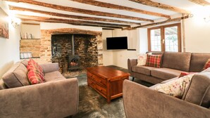 A cozy living room with exposed wooden beams, a stone fireplace, a flat-screen TV, and comfortable seating. - Lower West Curry Farmhouse (Launceston)