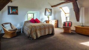 Un dormitorio acogedor en el ático, con una cama, una silla, un escritorio y una lámpara.