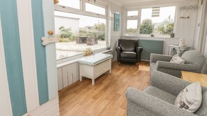 A cozy room with a window seat, a black leather chair, and two grey sofas. - Wagtail Cottage (Dumfries)