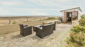 A patio with wicker furniture and a small building with a glass door. - Wagtail Cottage (Dumfries)
