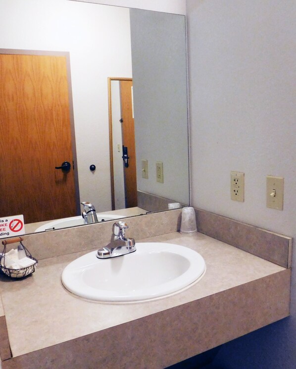 A bathroom with a white sink, a mirror, and a door. - Americas Best Value Inn Fredonia (Fredonia)