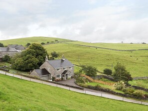 Paisaje rural con una casa de piedra, un muro de piedra y un campo cubierto de hierba.