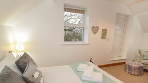 A bedroom with a bed, pillows, a quilted bedspread, a bedside lamp, a window, and a door. - Hen Stabl (Llanrwst)