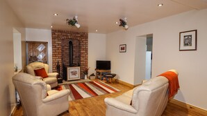 A living room with two leather armchairs, a brick fireplace, a flat-screen TV, and a wooden floor. - The Granary (Stoke-on-Trent)