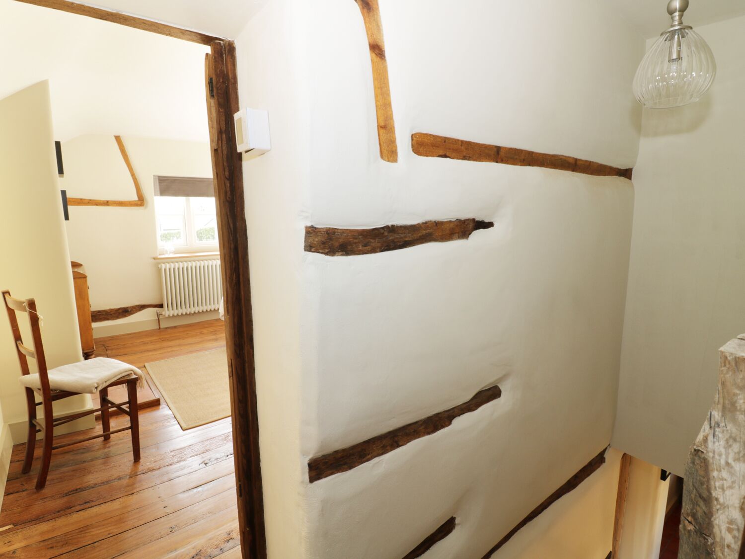 A room with exposed wooden beams, a radiator, a chair, and a hanging light fixture.