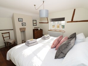Een slaapkamer met een groot bed, een kaptafel, een stoel en een raam met uitzicht op bomen.