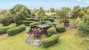 A cluster of wooden cabins surrounded by well-maintained hedges and trees, with a gravel path connecting them. - Oakwood House (Rhayader)