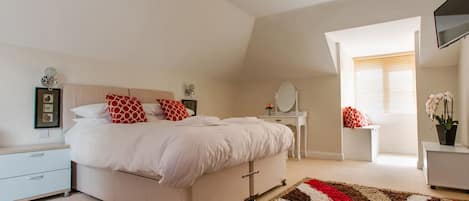 Quarto com cama, mesas de cabeceira, cômoda, espelho, janela com persianas e TV montada na parede.