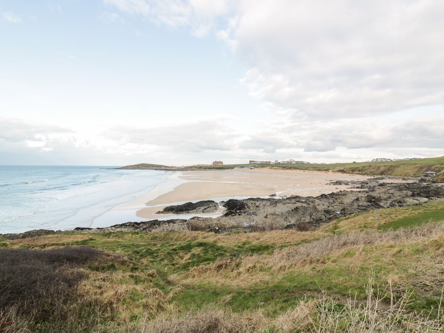 A coastal landscape with a beach, rocky outcrops, and a distant building.