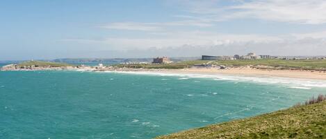A coastal landscape with a grassy hill, a beach, and buildings in the distance.