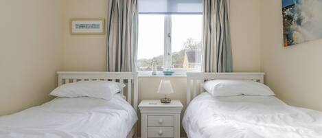 A bedroom with two single beds, a nightstand with a lamp, a framed picture on the wall, and a window with curtains.