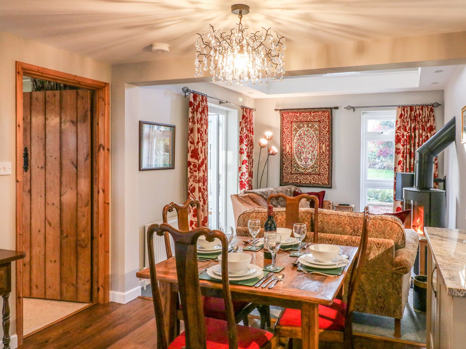 A dining area with a wooden table set for four, chairs, a chandelier, and a fireplace.
