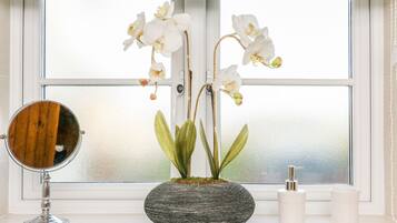 A bathroom with a window, a round mirror, a potted orchid, and two white candles on the windowsill.