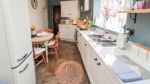 A compact kitchen with white cabinets, a wooden dining table, and a window with a view. - Chapel Cottage (Scarborough)