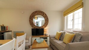 Un salon avec un canapé, un téléviseur, une table en bois et un miroir au mur.