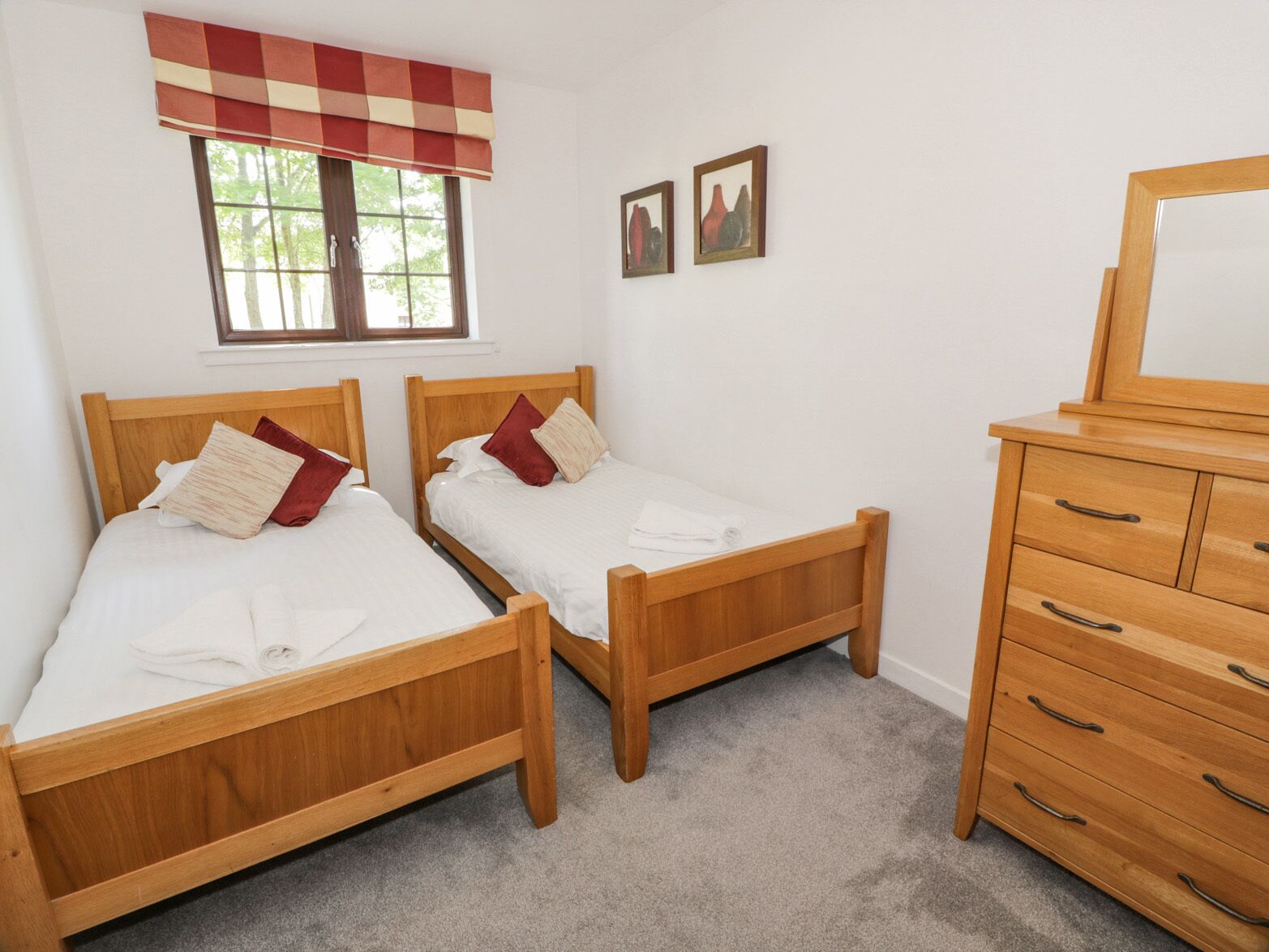 A bedroom with two wooden beds, a wooden dresser, and a window with a checkered valance.