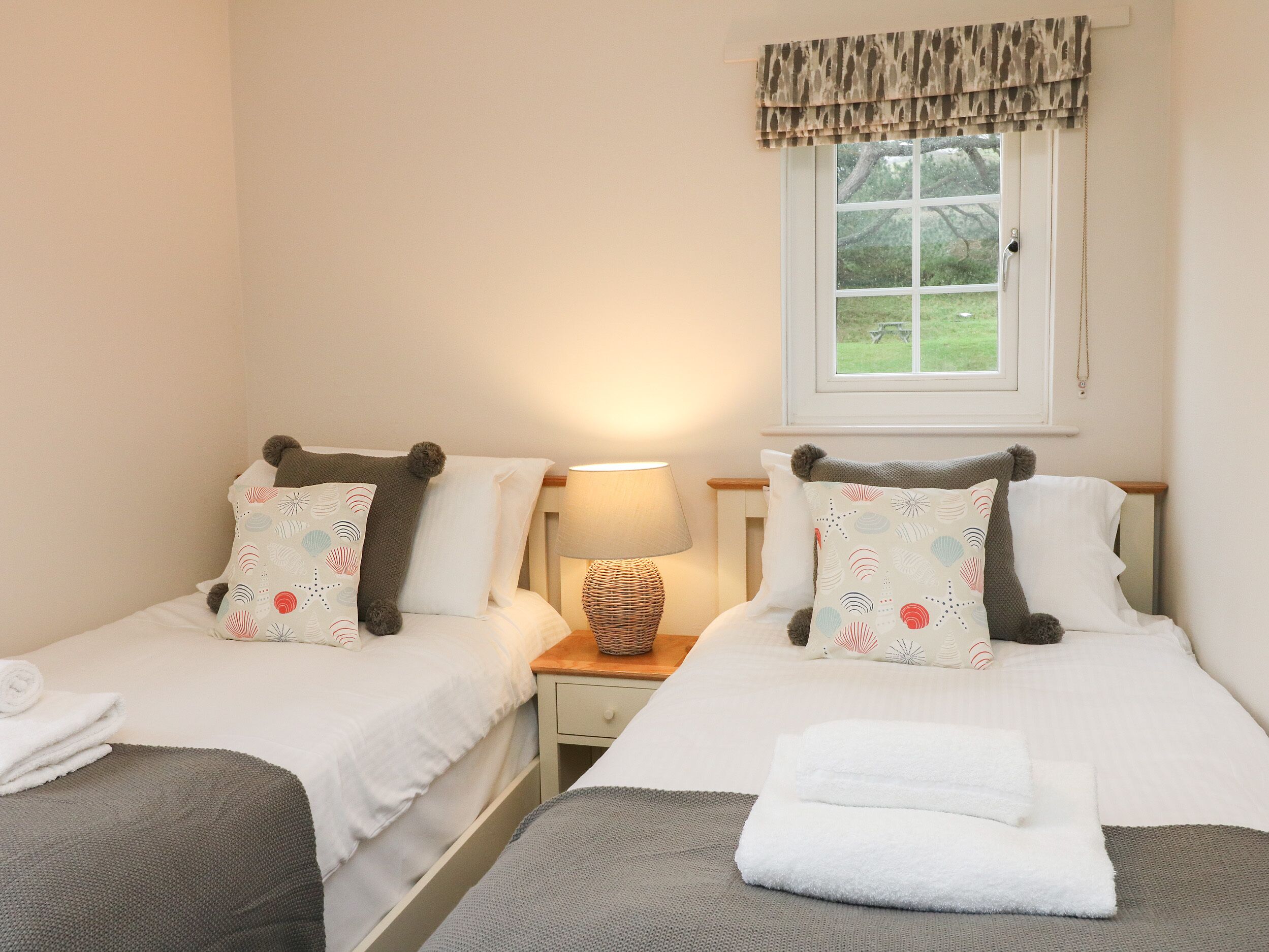 A twin room with two beds, each with a pillow and a bedside table with a lamp.