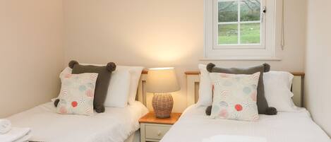 A twin room with two beds, each with a pillow and a bedside table with a lamp.