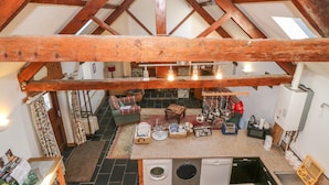 A rustic interior with exposed wooden beams, a fireplace, a kitchen with a washing machine, and a seating area with a rug. - Beudy Bach (Caernarfon)