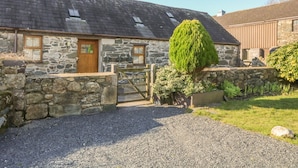 A stone building with a wooden door and a gravel driveway. - Beudy Bach (Caernarfon)