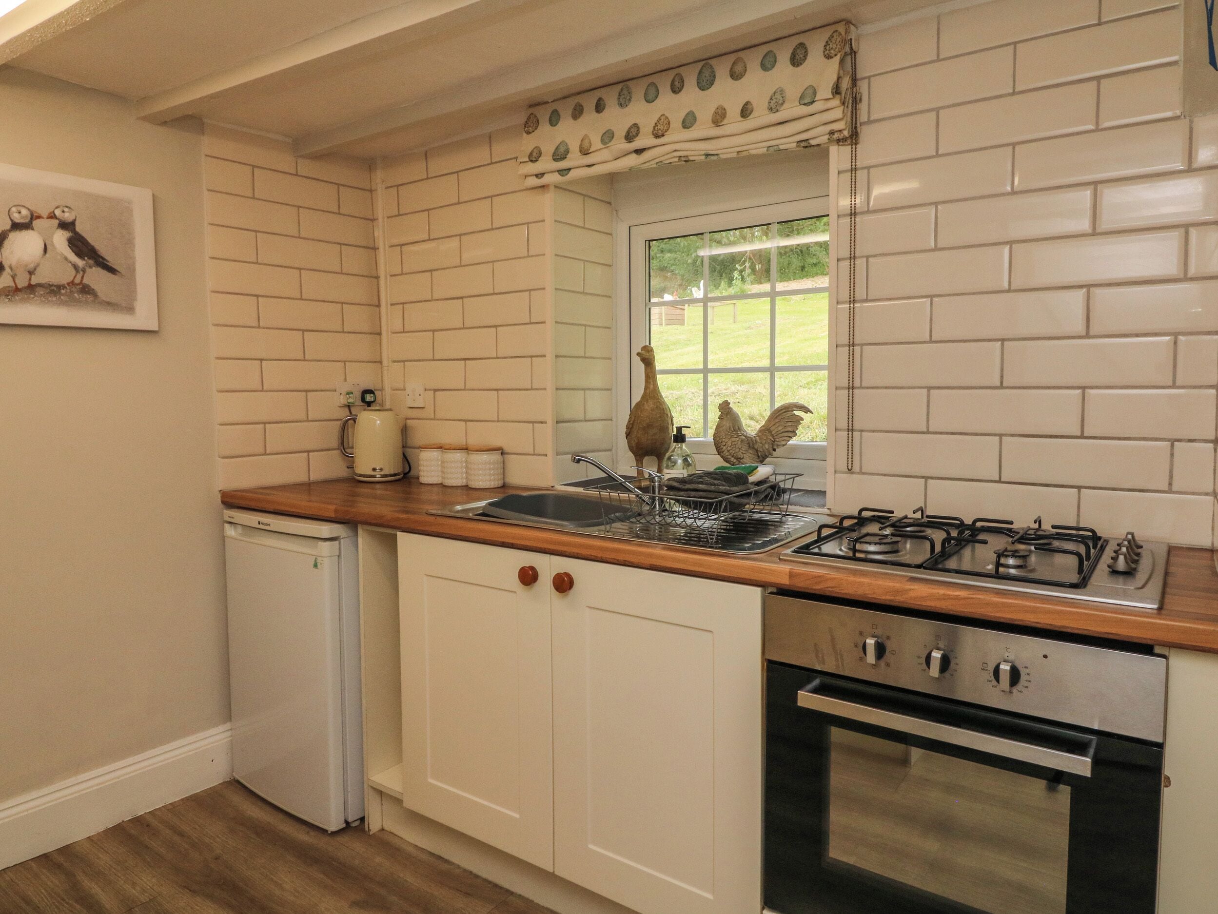 A kitchen with white tiled walls, a wooden countertop, a built-in oven, and a window with a view of greenery.