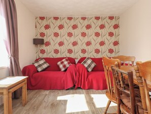 Una habitación acogedora con un sofá rojo, una mesa de madera y una silla de madera.